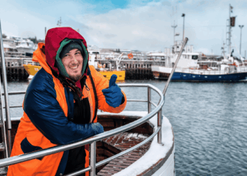 Giovane lavoratore marittimo in un porto artico con un peschereccio sullo sfondo